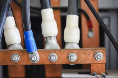 Elektrik bağlantısı. Sonunda beyaz ve mavi bir kılıfı olan siyah bir elektrik kablosu, güç dağıtım sisteminde önemli bir elektrik iletkeni olan bakır busbar 'a bağlıdır..