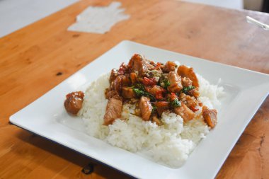 Üstünde kızartma tabağı olan kare beyaz tabak. Karıştırılmış porsiyonda kırmızı çan biberi ve taze yeşil otlar gibi sebzelerle birlikte muhtemelen domuz eti parçaları yer alıyor..