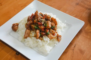 Üstünde kızartma tabağı olan kare beyaz tabak. Karıştırılmış porsiyonda kırmızı çan biberi ve taze yeşil otlar gibi sebzelerle birlikte muhtemelen domuz eti parçaları yer alıyor..