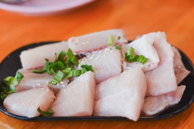 İnce dilimlenmiş tilapia masadaki siyah bir tabağa konmuş.