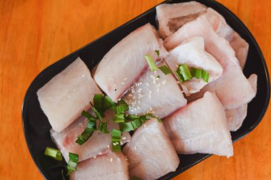 İnce dilimlenmiş tilapia masadaki siyah bir tabağa konmuş.