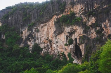 Yoğun yeşil ormanlarla kaplı büyük kireçtaşı dağlarının manzarası. Kireçtaşı dağları sarp kayalıklarla karakterize edilir, doğal çatlaklar ve çatlaklar farklı kaya katmanlarını ortaya çıkarır..