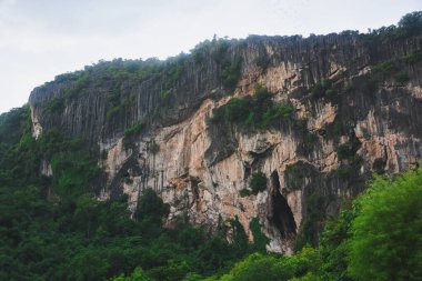 Yoğun yeşil ormanlarla kaplı büyük kireçtaşı dağlarının manzarası. Kireçtaşı dağları sarp kayalıklarla karakterize edilir, doğal çatlaklar ve çatlaklar farklı kaya katmanlarını ortaya çıkarır..