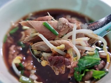 Duck soup in a bowl. Asian man's hand scooping up duck and bean sprouts with a spoon.