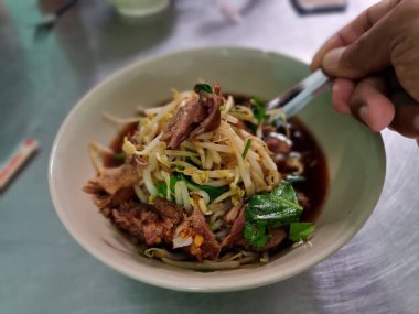 Duck soup in a bowl. Asian man's hand scooping up duck and bean sprouts with a spoon.