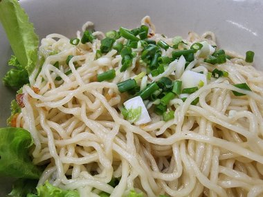 Taze doğranmış yeşil soğanla kaplanmış ve yanında beyaz bir kasede kıtır marul yaprakları bulunan iştah açıcı kuru eriştelerden oluşan bir porsiyon. Basit ama lezzetli bir yemek..