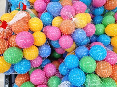 Pembe, mavi, sarı, yeşil ve turuncu gibi çok sayıda renkli plastik toplar beyaz ağ torbalarının içinde sıkıca paketlenmiştir. Parlak renkler ve ağ dokusu dinamik ve neşeli bir görüntü yaratıyor.