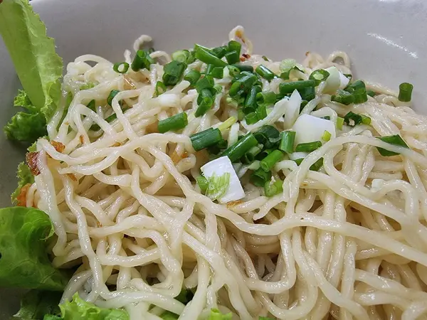 Taze doğranmış yeşil soğanla kaplanmış ve yanında beyaz bir kasede kıtır marul yaprakları bulunan iştah açıcı kuru eriştelerden oluşan bir porsiyon. Basit ama lezzetli bir yemek..