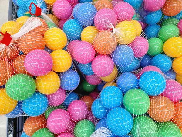 Pembe, mavi, sarı, yeşil ve turuncu gibi çok sayıda renkli plastik toplar beyaz ağ torbalarının içinde sıkıca paketlenmiştir. Parlak renkler ve ağ dokusu dinamik ve neşeli bir görüntü yaratıyor.
