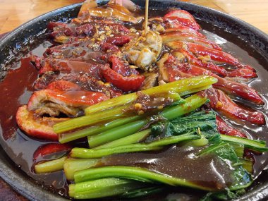 Zengin Çin sosuyla kaplanmış leziz kızarmış ördek dilimleri, taze yeşil sebzelerle birlikte cızırdayan bir elektrikli ocakta servis ediliyor..