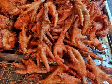 Metal tel bir tepside servis edilen kızarmış tavuk ayakları altın kahverengi dokularını sergiliyor ve eşsiz bir yemek pişirme zevki veriyor.