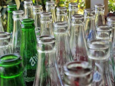 Yakından bakıldığında boş cam şişeler, yansımalar ve doğal ışıkla sıralanmış, dokuyu, deseni ve şeffaflığı çağrıştırıyor.