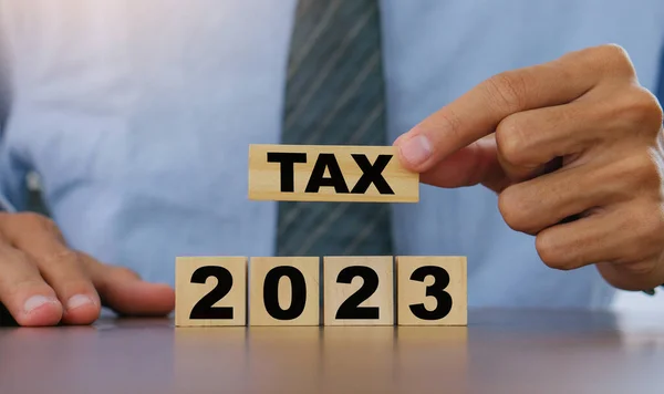 TAX in 2023 concept,Business man holding wooden block. State taxes,tax payment, governant ,finance, tax accounting, statistics and data analytic reserach,tax return, strategy plan, report.Business 2023 tax new year concept
