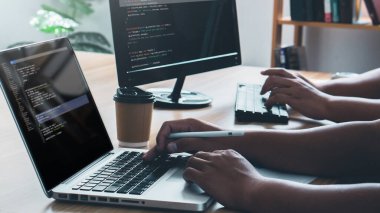Couple Young programmer writing program code sitting at the workplace with laptop and computer in the office.