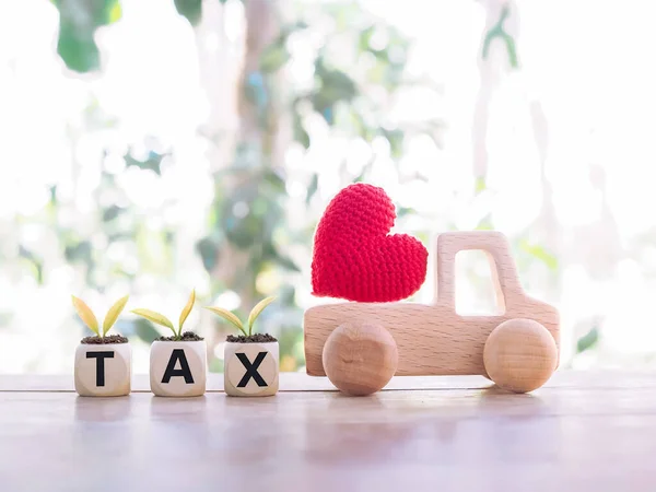 Red heart on wooden toy car and wooden blocks with the word TAX. The concept of paying tax for car. Car taxes.
