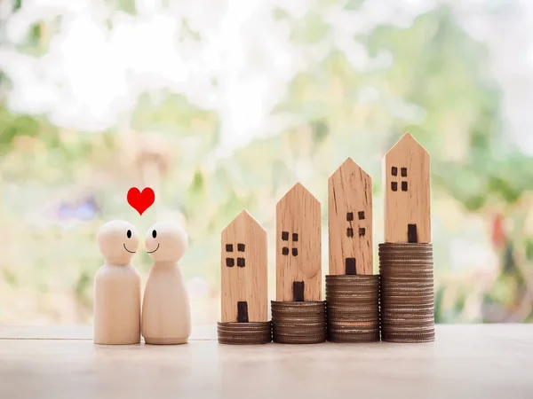 Wooden figure couple happy face with heart and miniature house on stack of coins for Investment property concept. Saving money for buy a house.