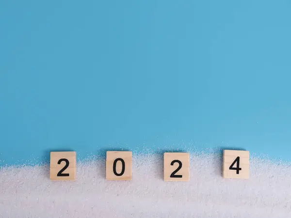 Wooden block with number 2024 and white sand on blue background. Top view with copy space for summer background. The concept for summer of new year 2024