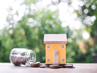 Bozuk para yığınının üzerinde minyatür bir ev. Ev için para biriktirme konsepti, emlak yatırımları, ev kredisi, gayrimenkul..