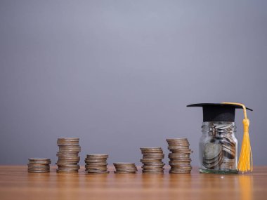 Mezuniyet şapkası ve bozuk paralarla dolu cam bir şişe. Eğitim için para biriktirme kavramı, öğrenci kredisi, burs, gelecek eğitim ücretleri