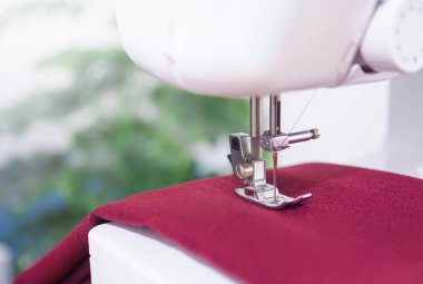 Kırmızı kumaşla çalışan dikiş makinesini kapatın, yeni elbiseler dikin.