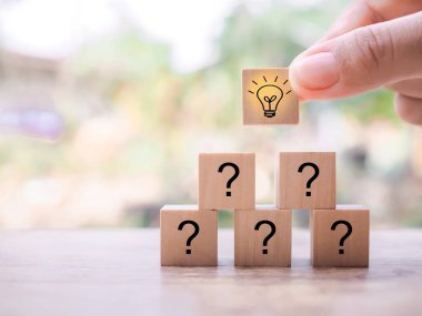 Close up hand arranging wooden block with light bulb and wooden block with question mark for leadership, creative, idea, innovation concept.
