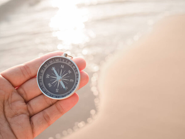 Close up hand holding compass with beach background