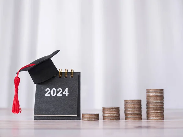 Study goals, 2024 Desk calendar with graduation hat and stack of coins. The concept of saving money for education, student loan, scholarship, tuition fees in New Year 2024