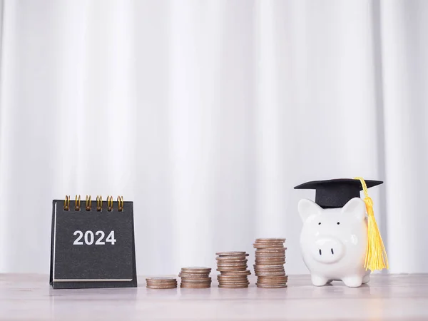 Study goals, 2024 Desk calendar, Piggy bank with graduation hat and stack of coins. The concept of saving money for education, student loan, scholarship, tuition fees in New Year 2024