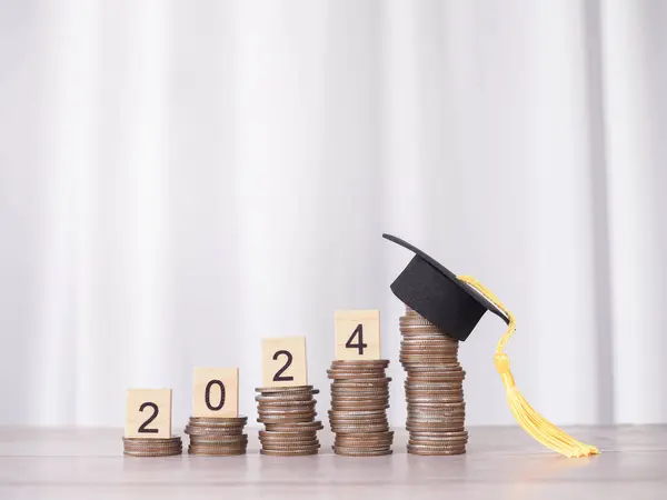 Study goals, Wooden block with number 2024 on stack of coins with graduation hat. The concept of saving money for education, student loan, scholarship, tuition fees in New Year 2024