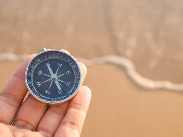 Close up hand holding compass with beach background