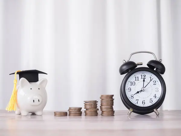 Piggy bank with graduation hat, stack of coins and black alarm. The concept of saving money and manage time for education, student loan, scholarship, tuition fees in future