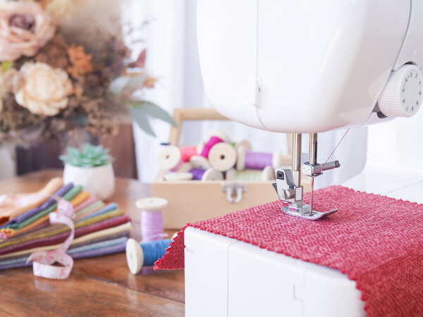 Close up sewing machine working with red fabric, sewing accessories on the table, stitch new clothing.