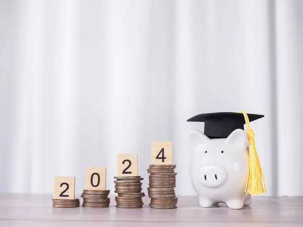 Study goals, Piggy bank with graduation hat and Wooden block with number 2024 on stack of coins. The concept of saving money for education, student loan, scholarship, tuition fees in New Year 2024