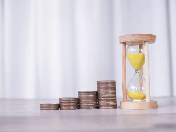 Hourglass and stack of coins. The concept of saving money, manage time to business achievement goal, Financial, Investment and Business growing in new year 2024.