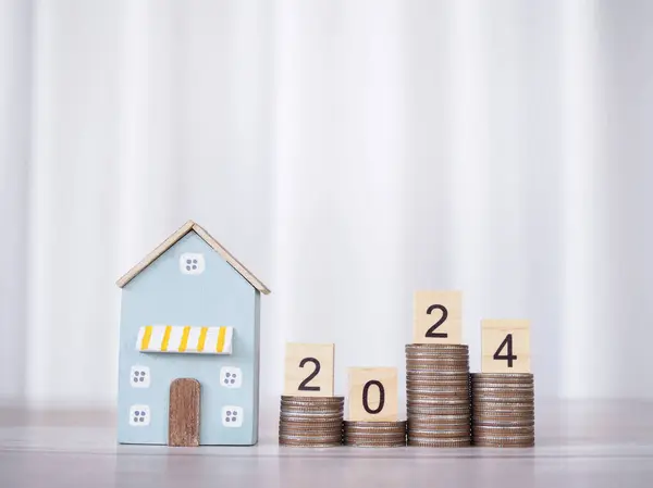 Miniature house, Wooden blocks with number 2024 on stack of coins. The concept of payment tax for house, Property investment, House mortgage, Real estate in New Year 2024.