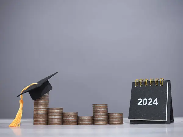 stock image 2024 desk calendar and graduation hat on stack of coins. The concept of saving money for education, student loan, scholarship, tuition fees in Year 2024