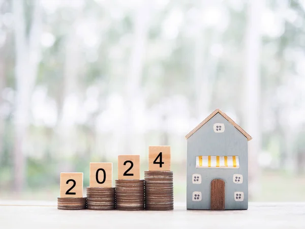 Miniature house, Wooden blocks with number 2024 on stack of coins. The concept of payment tax for house, Property investment, House mortgage, Real estate in New Year 2024.