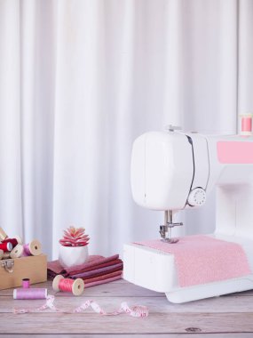 Pembe kumaşla çalışan dikiş makinesini kapatın, masaya aksesuarlar dikin, yeni kıyafetler dikin..