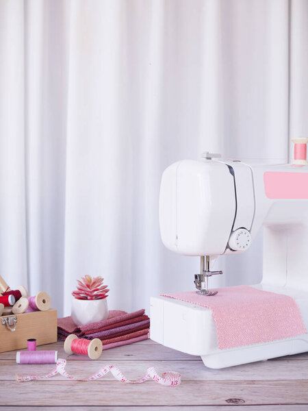 Закрыть швейную машинку, работающую с розовой тканью, шить аксессуары на столе, шить новую одежду.
