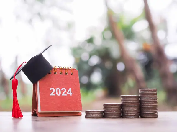 Study goals, 2024 Desk calendar with graduation hat and stack of coins. The concept of saving money for education, student loan, scholarship, tuition fees and manage time to success graduate.