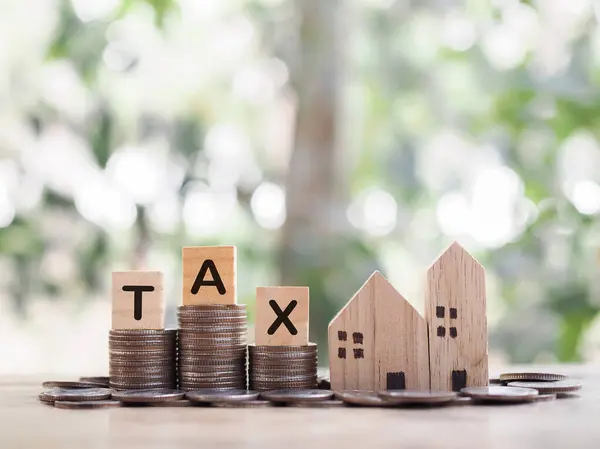 Miniature house and Wooden blocks with the word TAX on stack of coins. The concept of payment tax for house, Property investment, House mortgage, Real estate