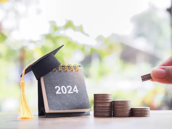 Study goals, 2024 Desk calendar with graduation hat and stack of coins. The concept of saving money for education, student loan, scholarship, tuition fees and manage time to success graduate