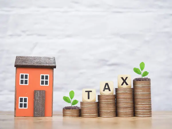 Miniature house and Wooden blocks with the word TAX on stack of coins. The concept of payment tax for house, Property investment, House mortgage, Real estate