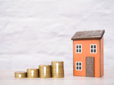 Minyatür ev ve oklu bozuk para yığını. Ev fiyatları, emlak yatırımları, ev kredisi, gayrimenkul.