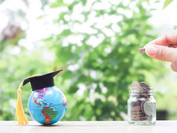 Stock image Close up hand putting coin into glass bottle and Earth globe with graduation hat. The concept of saving money for education, student loan, scholarship, tuition fees in the future