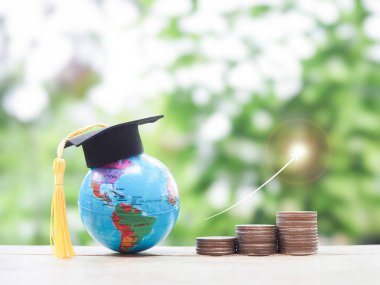 Mezuniyet şapkalı dünya küresi ve yükselen oklu bozuk para yığını. Eğitim, öğrenci kredisi, burs, eğitim ücretleri için para biriktirme kavramı