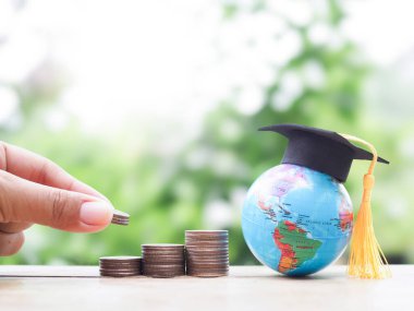 Yakın el, bozuk para yığınına ve mezuniyet şapkasıyla Dünya küresinin içine para koyuyor. Eğitim, öğrenci kredisi, burs, eğitim ücretleri için para biriktirme kavramı