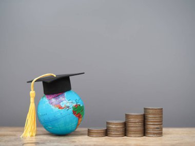 Mezuniyet şapkası ve bozuk paralarla dolu bir dünya küresi. Eğitim, öğrenci kredisi, burs, eğitim ücretleri için para biriktirme kavramı