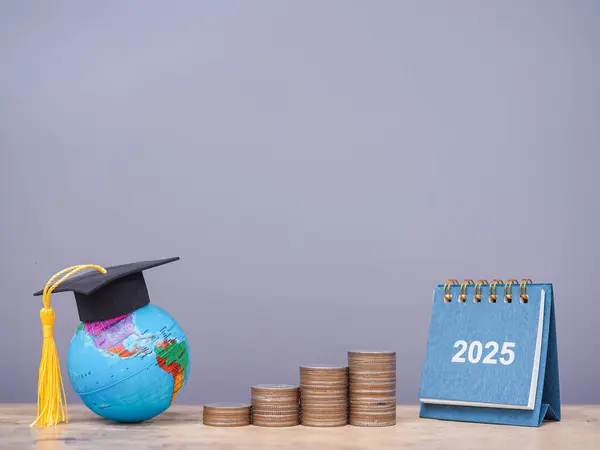 2025 masa takvimi, mezuniyet şapkası ve bozuk para yığınıyla Dünya küresi. 2025 yılında eğitim, öğrenci kredisi, burs, öğrenim ücreti için para biriktirme kavramı