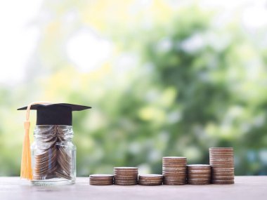 Mezuniyet şapkası ve bozuk paralarla dolu cam bir şişe. Eğitim için para biriktirme kavramı, öğrenci kredisi, burs, gelecekte öğrenim ücretleri
